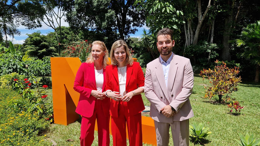 Foto van drie mensen voor oranje NL-letters