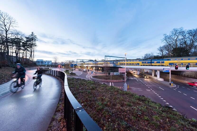 Fietsers bij station Driebergen-Zeist. Over het spoorviaduct rijdt een trein.